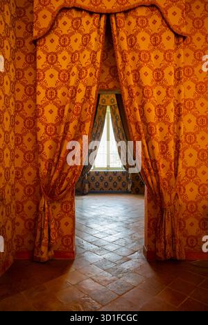 Luxurious vintage interior showing ornate patterned curtains leading to sunlit room with golden walls and classic tiled floor. Stock Photo