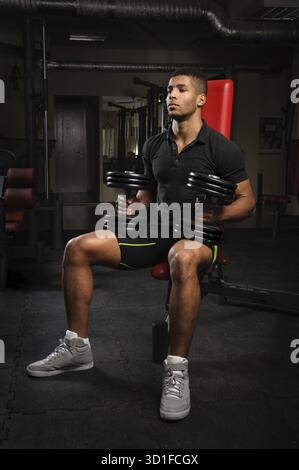 Handsome young african descent Mixed-race man sitting and resting on bench in gym Stock Photo
