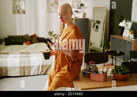 Young Adult Woman with Alopecia Listening to Music and Using Smartphone Stock Photo
