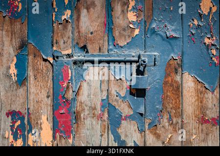 Vintage rusty deadbolt with padlock on the old wooden door. Horizontal closeup.  Cracked paint in several layers. Stock Photo