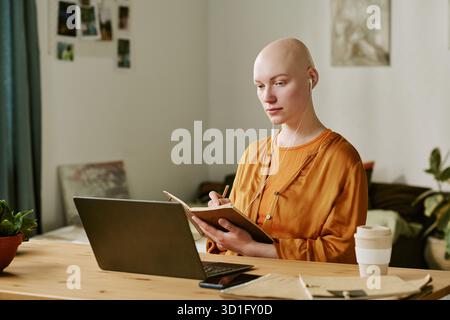 Young Adult Woman with Alopecia Writing Notes While Using Laptop Stock Photo