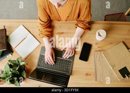Young Adult Woman Working on Laptop While Sitting at Wooden Desk Stock Photo