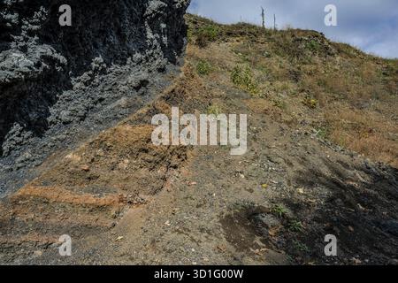 The scene shows different layers of earth and rock formations in a rural area on a clear day. Dry grass and small plants are visible. zelezna hUrka Stock Photo