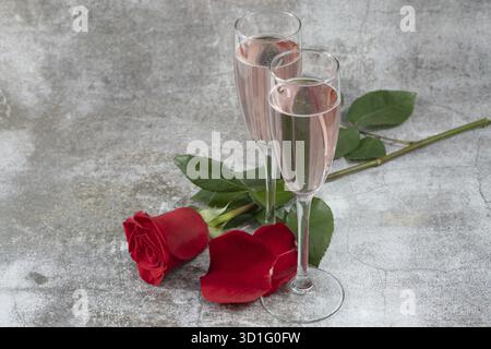 Two glasses of champagne and a red rose isolated on a gray table Stock Photo
