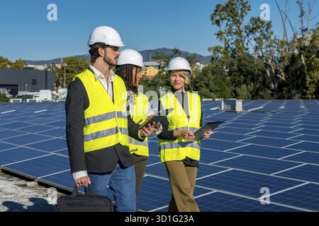Team of diverse engineers and technicians wearing hard hats and high visibility vests inspecting a large array of solar panels on a rooftop, symbolizi Stock Photo