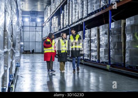 Diverse logistics team is walking and discussing inventory management within a modern cold storage warehouse, ensuring efficient operations for frozen Stock Photo