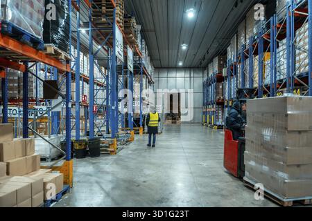 Workers are moving inventory using a forklift and inspecting goods on high racks in a large cold storage logistics warehouse, ensuring efficient opera Stock Photo
