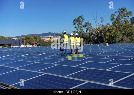 Team of engineers is inspecting an array of solar panels on a rooftop power plant, working on a sustainable energy solution and using renewable techno Stock Photo