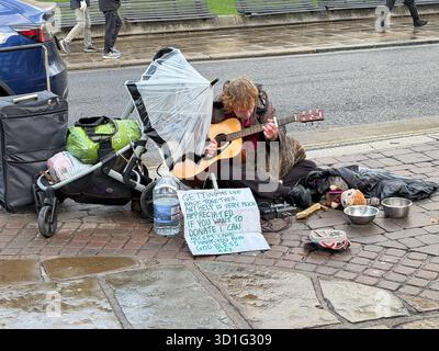 Windsor, Berkshire, UK. 25th October, 2025. A homeless man sits with his dog on a wet pavement opposite Windsor Castle in Windsor, Berkshire as he plays his guitar. The number of homeless British people sleeping rough remains high. Many UK residents are frustrated at how many people are homeless whilst illegal migrants coming into the UK on boats are often housed in 4 star hotels with food, clothes, money, mobile phones and entertainment provided for them. Credit: Maureen McLean/Alamy Stock Photo