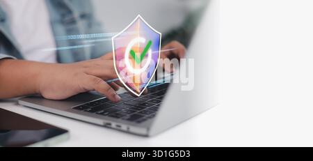 Person typing on laptop with digital shield and green check icon. Concept of cybersecurity, data protection, safe internet, antivirus, and secure onli Stock Photo