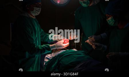 Professional Medical Doctors and team performing surgical operation in bright Modern operating room with lighting equipment in hospital. Stock Photo