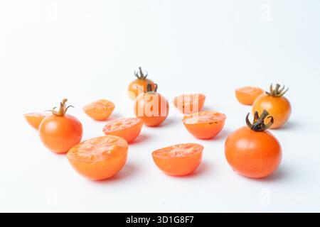 Fresh cherry tomatoes, whole and sliced, scattered on a clean white background. Minimalist food concept with ample copy space. Healthy ingredients. Stock Photo