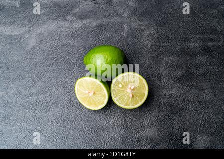Close-up of fresh green limes, whole and sliced. The citrus fruit is on a rustic wooden cutting board with a dark, textured background. Stock Photo