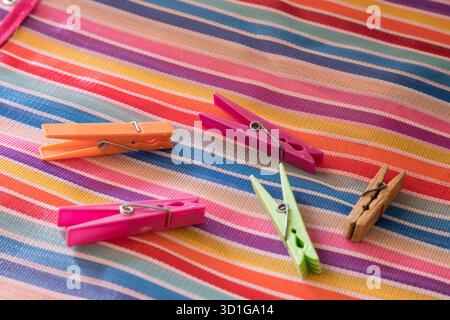 A vibrant range of colorful wooden clothes pegs on a background with horizontal stripes in various colors, creating a cheerful and energetic visual ef Stock Photo