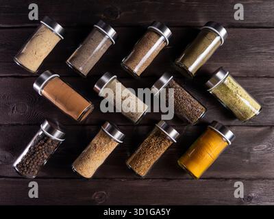 Collection of various spices and seasonings neatly arranged in glass jars. The jars are placed on a wooden surface against a dark background, highligh Stock Photo