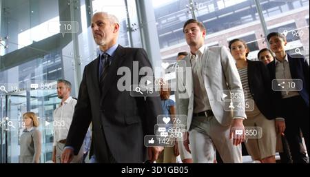 Striding grey-haired leader guiding team in suits through glass atrium with social media overlays Stock Photo