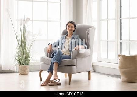 Full length portrait happy older woman relaxing in comfy armchair Stock Photo