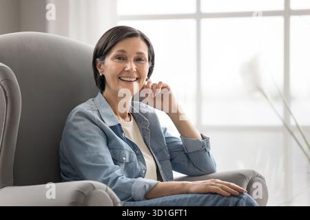 Portrait relaxed mature lady smiling at camera in comfy armchair Stock Photo