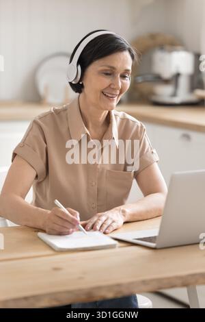 Happy older lady in headphones listening to lecture using notebook Stock Photo