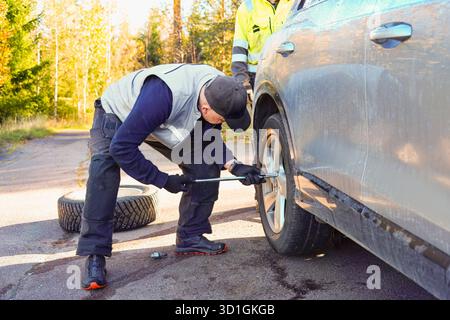 Male automotive technician is working on changing a tire on a vehicle by the roadside, demonstrating practical skills in a serene outdoor environment Stock Photo