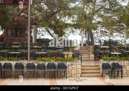 Empty plastic chairs and tables arranged neatly in an outdoor restaurant setting, surrounded by plants and trees, creating a peaceful and inviting atm Stock Photo