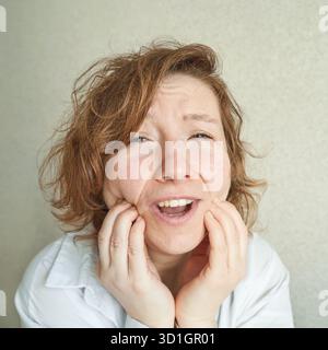 Female caucasian adult with surprised expression and tousled hair in white shirt against beige background. Stock Photo