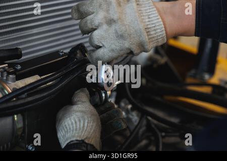 A person is diligently working on a car engine using a wrench, adjusting components for better performance and maintenance upkeep Stock Photo