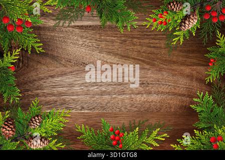 Rustic Christmas border made of conifer branches, cones and red berries on brown wooden background. Stock Photo