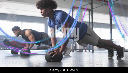Doing push-ups man in athletic clothes balancing on medicine ball in gym room with pull-up rig Stock Photo