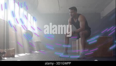 Sitting muscular man wearing black tank top on plyometric box in fitness studio, with medicine ball Stock Photo