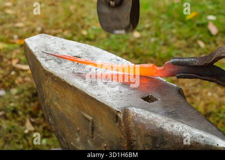 Close-up of a blacksmith working on a glowing piece of hot metal with tongs and hammer over an anvil. The photo highlights craftsmanship, heat, and tr Stock Photo
