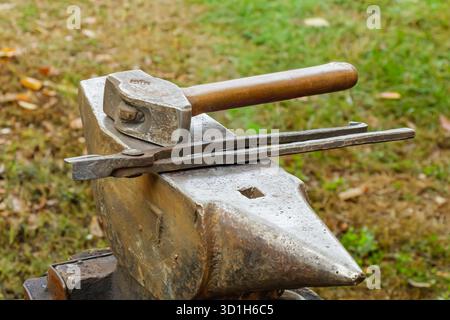 A close-up view of blacksmithing tools—a hammer and tongs—placed on a solid metal anvil outdoors. The image captures the essence of traditional crafts Stock Photo
