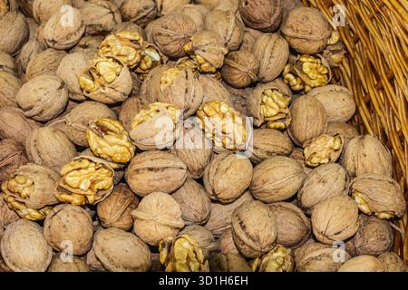 Close-up of walnuts in their shells, some cracked open to reveal the kernels, placed in a rustic wicker basket. The photo highlights the texture, eart Stock Photo