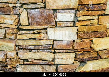 Close-up of a rustic stone wall built from uneven natural rocks in shades of brown, beige, and ochre. The detailed texture and earthy colors highlight Stock Photo