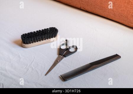 A classic wooden hair brush, professional black hairdressing scissors, and a dark comb are neatly arranged on a clean white fabric surface, highlighti Stock Photo