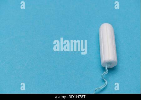 Close view of a white tampon on a vibrant blue surface. Stock Photo