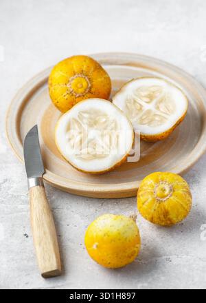 Fresh lemon cucumbers on a ceramic plate, one cut in half showing juicy white flesh and seeds. Natural light still life of organic produce Stock Photo