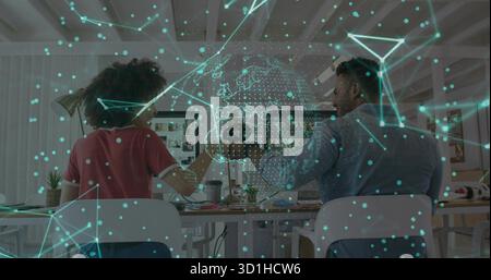 Pair of developers collaborating at open office desk, with dual monitors and holographic globe Stock Photo