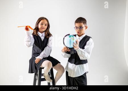 Two Caucasian children engaged in imaginative play. A girl holding a paper airplane and a boy examining a globe. Stock Photo