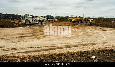 Construction site in Dublin, Ireland with heavy machinery, dump trucks, and earth movers preparing ground for development under cloudy skies. Stock Photo
