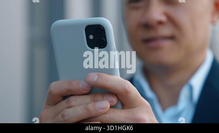 Close up male hands holding mobile phone Asian middle-aged business man using cellphone chatting texting with smartphone in city Korean businessman Stock Photo