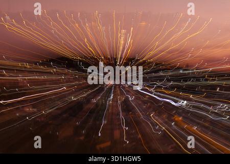 Abstract long exposure city lights at dusk creating zoom burst effect with dynamic motion trails, orange sky and glowing urban energy at sunset Stock Photo