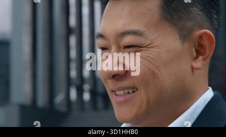 Happy smiling Asian middle-aged business man messaging with mobile phone app in city Japanese businessman using smartphone service chat online Stock Photo