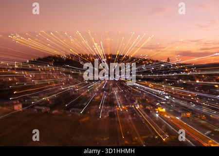 Abstract long exposure city lights at dusk creating zoom burst effect with dynamic motion trails, orange sky and glowing urban energy at sunset Stock Photo