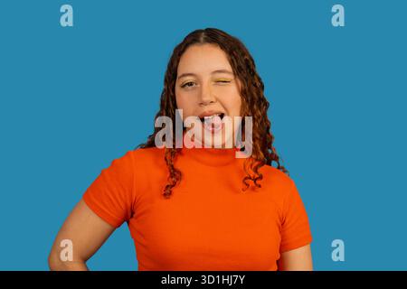 Playful young woman winking and sticking out tongue on a blue background Stock Photo
