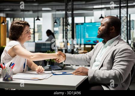 Confident male candidate receives a warm welcome from the HR manager after being accepted, both shake hands in agreement and prepare for employment paperwork and team integration. Stock Photo