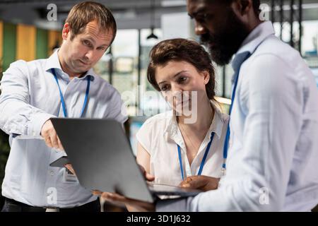 Diverse employees in modern office, drafting reports and collaborating on strategic planning. Multiethnic professionals reviewing data on laptop to support business progress and innovation. Stock Photo
