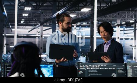 Data center manager supervising work done by programmers working on neural network software. Server hub supervisor overseeing IT staff members implementing deep learning tech, camera A Stock Photo