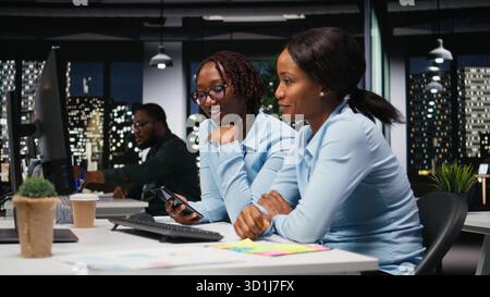 Black women working together with data insights on desktop in workspace, developing business solutions with strategy planning and performance metrics analysis for new goals achievement. Stock Photo