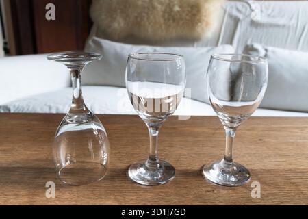 three clear, empty wine glasses – one inverted, two upright – arranged on a warm, textured wooden table with a soft focus background. Stock Photo